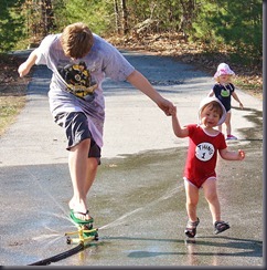 Sebastian jumps the sprinkler while Theodore joyfully holds on.